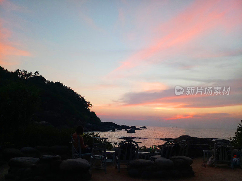 令人惊叹的海滩日落剪影与粉红色的天空和云彩，岩石山，桌子和椅子面对壮观的太阳和日出/日落在Palolem海滩，印度南部果阿，户外座位的海滩/海岸